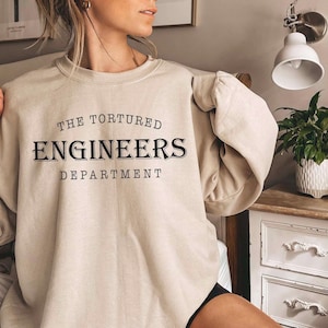 May include: A beige sweatshirt with the text "The Tortured Engineers Department" printed in black.