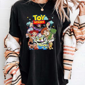 May include: Black t-shirt with a colourful graphic of characters from the animated film "Toy Story." The design includes Woody, Buzz Lightyear, and other beloved characters. The words "Toy Story" are displayed in a vibrant, eye-catching font.