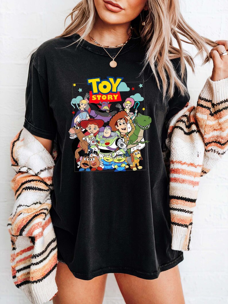 May include: Black t-shirt with a colourful graphic of characters from the animated film "Toy Story." The design includes Woody, Buzz Lightyear, and other beloved characters. The words "Toy Story" are displayed in a vibrant, eye-catching font.