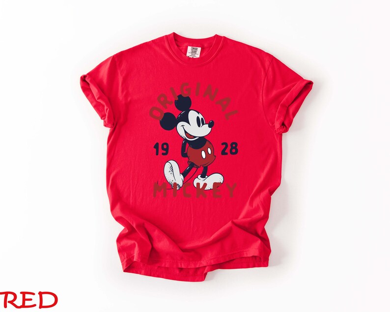 May include: A red t-shirt featuring a graphic of Mickey Mouse with the words "ORIGINAL 1928 MICKEY" in a circular design. The cartoon character is depicted in black, white, and red. The shirt is a solid red color.