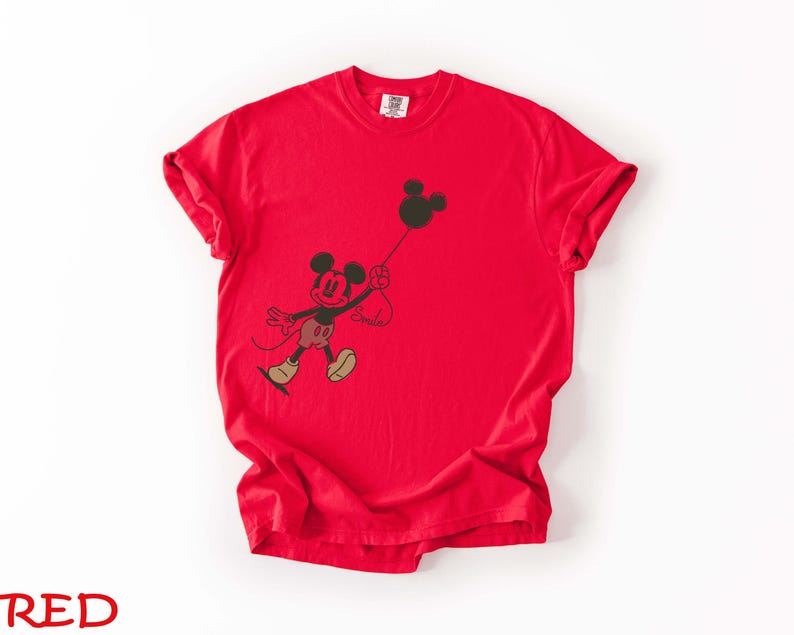 May include: A vibrant red t-shirt with a black graphic of Mickey Mouse holding a balloon. The cartoon character is wearing red shorts, yellow shoes, and a black face. The word "Smile" is written on the shirt.