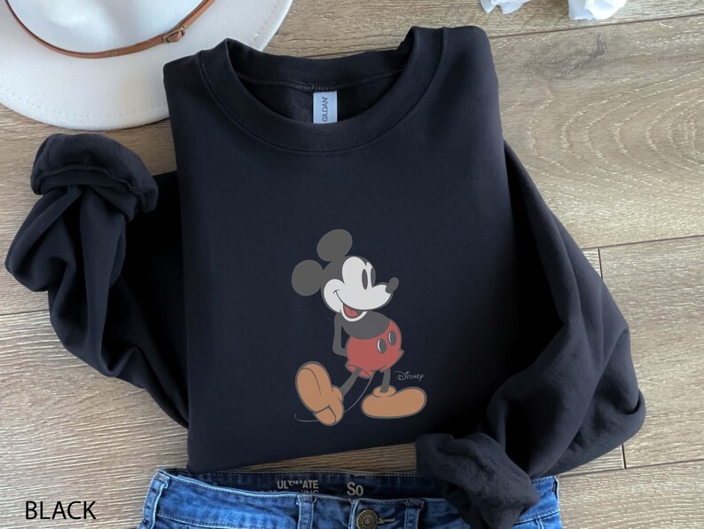 May include: Black crewneck sweatshirt featuring a Mickey Mouse graphic. The cartoon character is depicted in a classic pose, wearing red shorts and yellow shoes. The word "Disney" is printed below the character. The word "BLACK" is printed at the bottom.