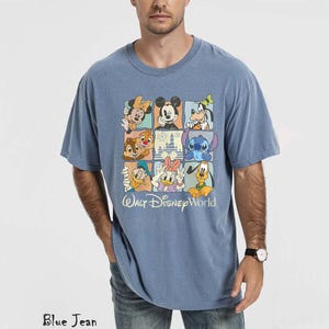 Op de afbeelding: Blauw T-shirt met een kleurrijke afbeelding van Disney-personages in een rasterpatroon. Het ontwerp bevat Mickey Mouse, Minnie Mouse, Donald Duck en Stitch. De tekst "Walt Disney World" staat eronder.