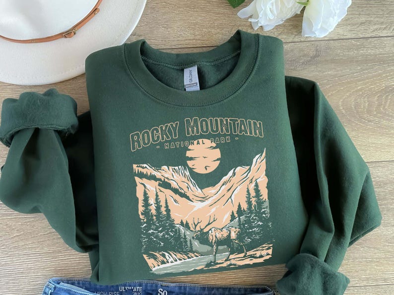 Pu&ograve; includere: Una felpa verde scuro con una stampa grafica di una catena montuosa e il testo "Rocky Mountain - National Park -" in bianco.