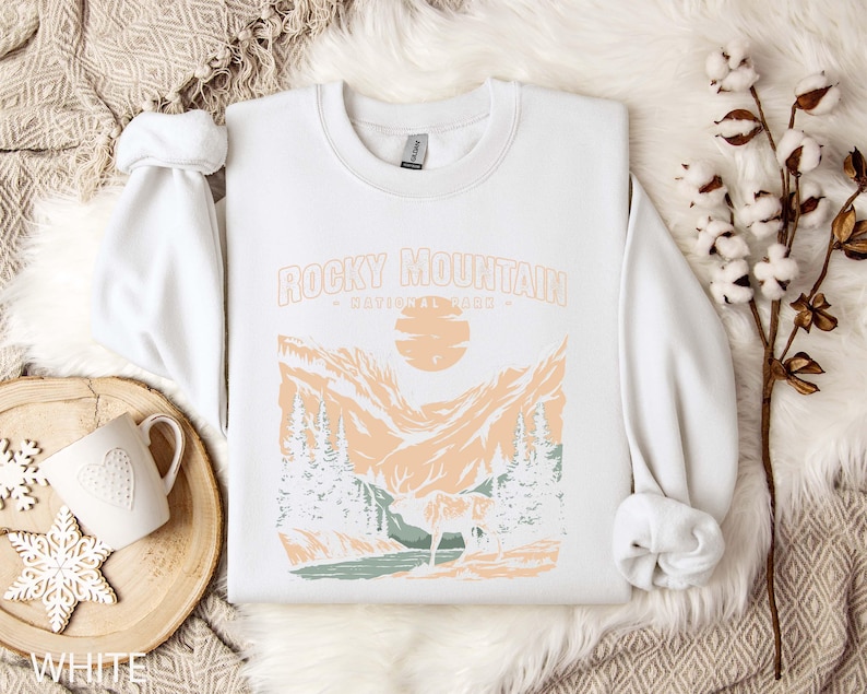 Pu&ograve; includere: Felpa bianca con una stampa grafica di una catena montuosa e il testo "Rocky Mountain National Park".
