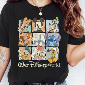 Op de afbeelding: Zwart T-shirt met een kleurrijk raster van Disney-personages, waaronder Mickey Mouse, Minnie Mouse, Goofy en Stitch. De tekst "Walt Disney World" staat eronder in een sierlijk lettertype.