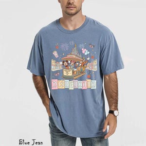May include: Blue short-sleeved t-shirt with a Disneyland graphic. The graphic features a trolley with Mickey Mouse, Donald Duck, and other characters, along with the word "Disneyland" in colorful letters. The shirt is a relaxed fit.