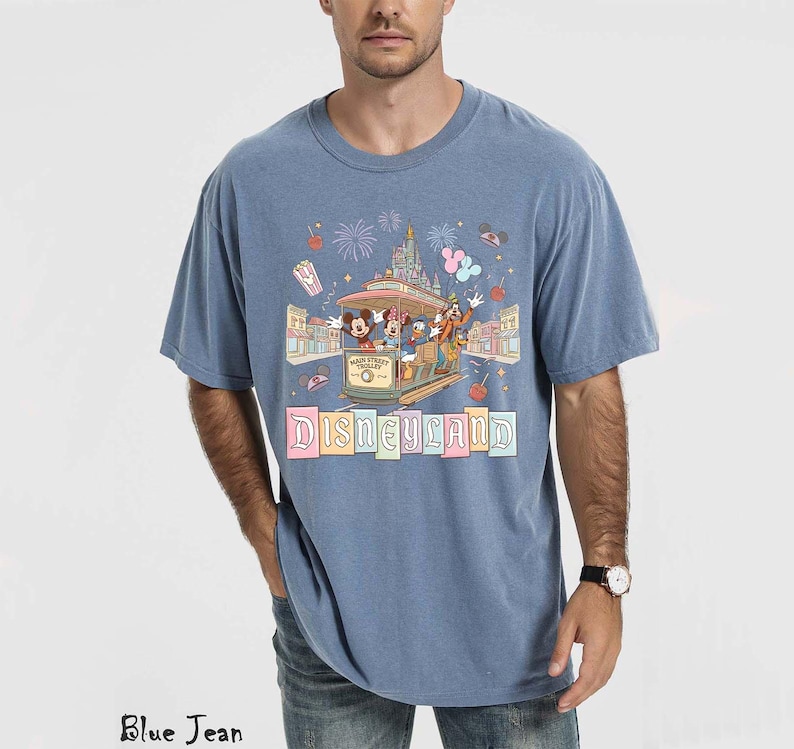 May include: Blue short-sleeved t-shirt with a Disneyland graphic. The graphic features a trolley with Mickey Mouse, Donald Duck, and other characters, along with the word "Disneyland" in colorful letters. The shirt is a relaxed fit.