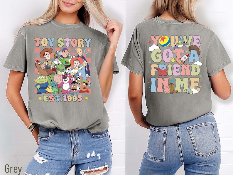 Może przedstawiać: Dwie szare koszulki z grafiką z Toy Story. Pierwsza koszulka zawiera napis "Toy Story" i obraz Woody'ego, Buzza Astrala i innych postaci z filmu. Druga koszulka zawiera napis "You've Got a Friend in Me" w kolorowej, retro czcionce.