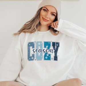 May include: White sweatshirt with a blue and white graphic that says "Cozy season" with snowflakes.