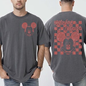 May include: Charcoal gray t-shirt featuring a distressed red Mickey Mouse graphic on the front and back. The back design includes a checkered pattern and the words "Mickey Mouse". The shirt has a vintage, worn look.
