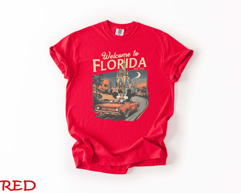 May include: A red t-shirt with a graphic that says "Welcome to Florida" and "Est. 1971". The graphic features a vintage car with Mickey and Minnie Mouse in front of a castle and palm trees.