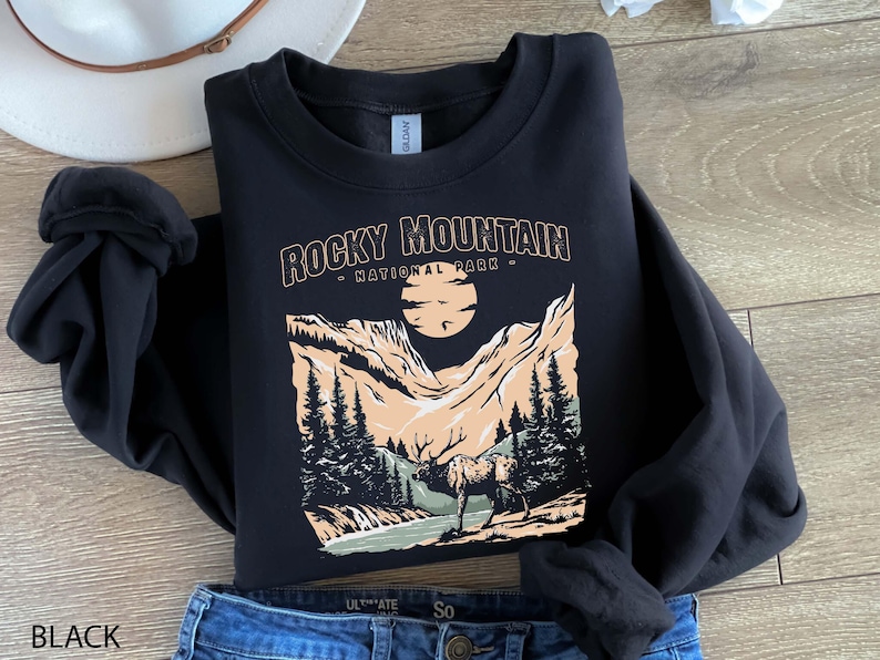 Pu&ograve; includere: Felpa nera con una stampa grafica di una catena montuosa e un cervo. Il testo "Rocky Mountain - National Park -" &egrave; stampato sulla felpa.
