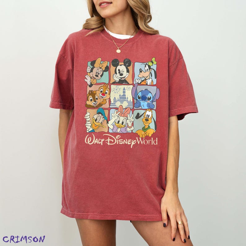 Op de afbeelding: Rood T-shirt met een rasterontwerp met Disney-personages zoals Mickey Mouse, Minnie Mouse, Goofy, Donald Duck en Stitch. De woorden "Walt Disney World" zijn in cursieve letters onder het raster gedrukt.
