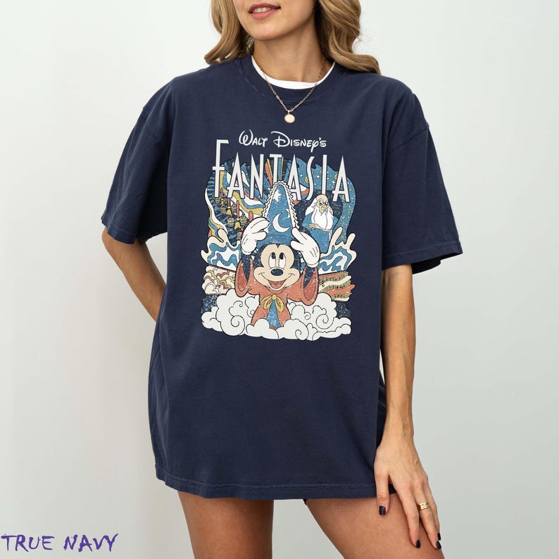 May include: A navy blue t-shirt with the words "Walt Disney's Fantasia" and a graphic of Mickey Mouse in a sorcerer's hat. The design includes clouds, stars, and characters from the film. The t-shirt has a loose fit.
