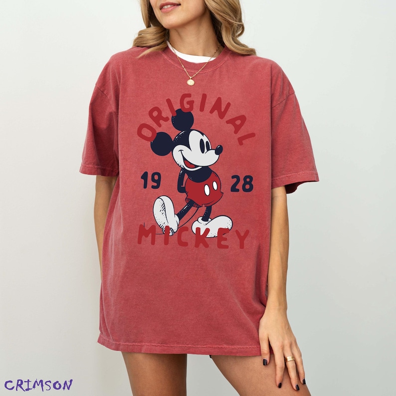 May include: Red t-shirt featuring a graphic of Mickey Mouse with the text "ORIGINAL MICKEY 1928". The design includes Mickey in his classic outfit. The shirt is a relaxed fit.