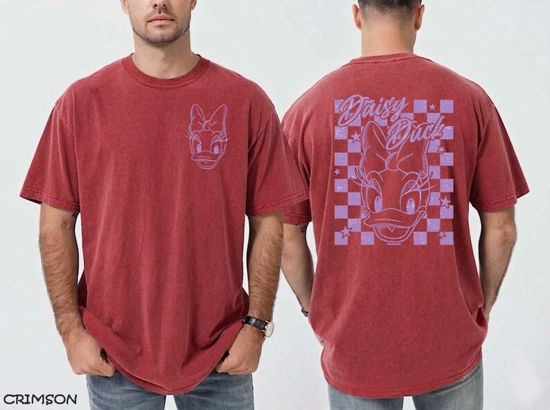 May include: Crimson red t-shirt featuring a Daisy Duck graphic. The front of the shirt has a small Daisy Duck outline, while the back displays a larger design with the words "Daisy Duck" and a checkered pattern. The shirt is a relaxed fit.