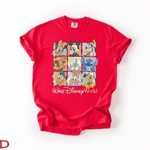 Op de afbeelding: Een rood T-shirt met een raster van Disney-personages, waaronder Mickey Mouse, Minnie Mouse, Donald Duck en Stitch. De woorden "Walt Disney World" staan eronder gedrukt. Het shirt is gemaakt van een zacht materiaal.