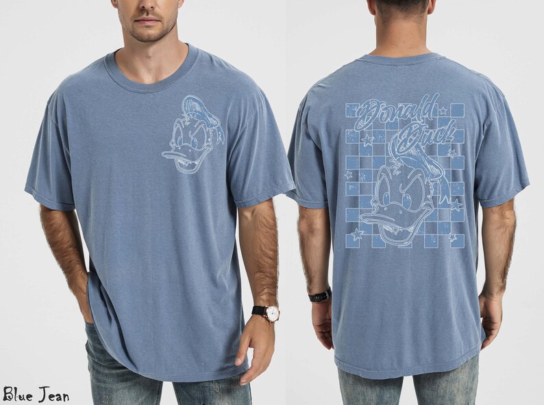May include: Blue jean-colored t-shirt featuring a Donald Duck graphic on the front and back. The front graphic is a detailed outline of Donald Duck. The back graphic includes the words "Donald Duck" and a checkered pattern.