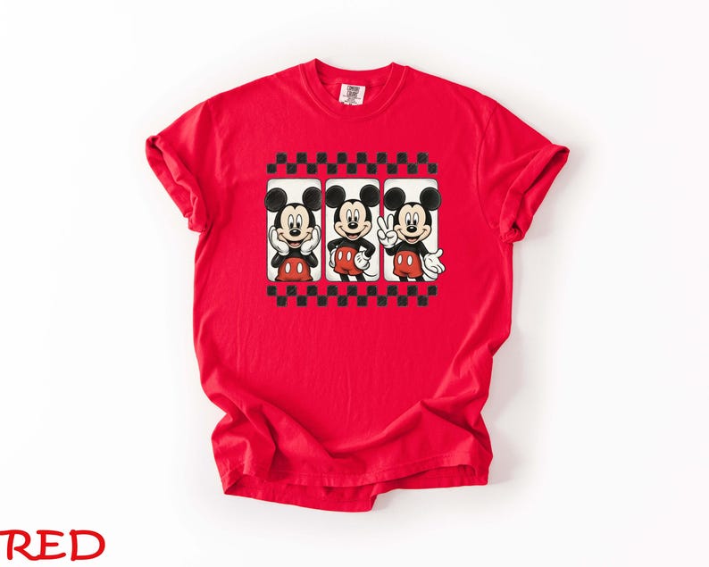 May include: A red t-shirt featuring three Mickey Mouse images in a black and white checkered frame. Mickey is depicted in various poses, wearing his signature red shorts and white gloves. The word "RED" is printed at the bottom.