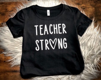 May include: Black t-shirt with white text that reads "Teacher Strong" with a heart in the word "Strong".