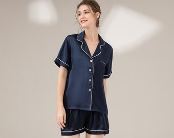 May include: A navy blue silk pajama set with short sleeves and shorts. The set has white piping around the collar, cuffs, and pockets.