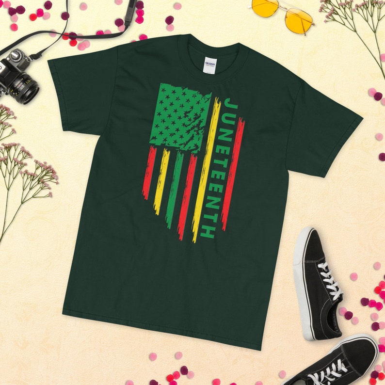 May include: A dark green t-shirt featuring a distressed American flag design in red, yellow, and green. The text "Juneteenth" is printed vertically on the right side of the flag.