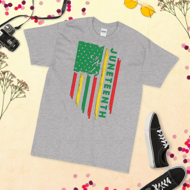 May include: A grey t-shirt featuring a distressed American flag design in green, yellow and red. The word "Juneteenth" is written vertically on the right side of the flag.