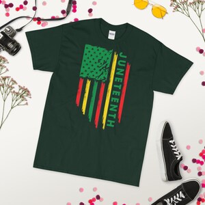 May include: A dark green t-shirt featuring a distressed American flag design in red, yellow, and green. The text "Juneteenth" is written vertically on the right side of the flag.