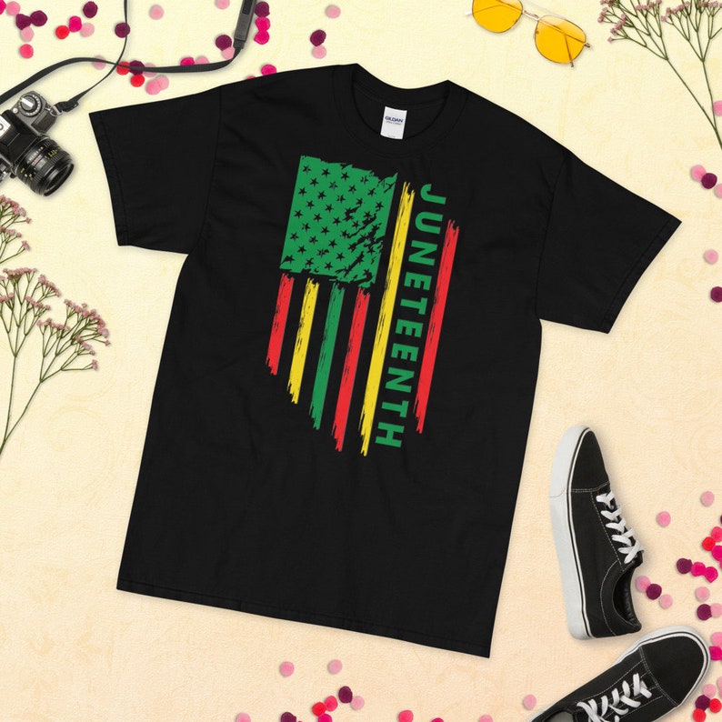 May include: Black t-shirt featuring a distressed American flag design in green, red and yellow. The text "Juneteenth" is written vertically on the right side of the flag.