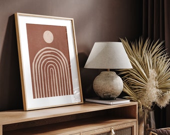 May include: A wooden media console with two drawers featuring a woven rattan front. The console has a light wood finish and is decorated with a framed abstract print of a sun and arches in shades of brown and cream. A lamp with a linen shade and a ceramic base sits on top of the console.