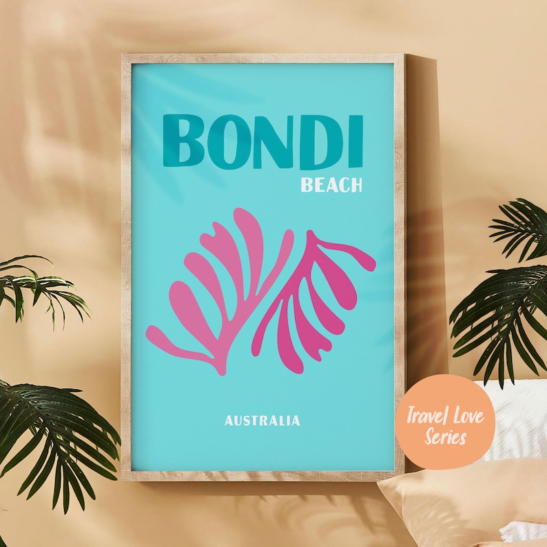May include: A turquoise blue poster with the text "BONDI BEACH AUSTRALIA" in white. The poster features a pink stylized leaf design. The poster is framed in a light wood frame. The text "Travel Love Series" is in a peach circle in the bottom right corner.