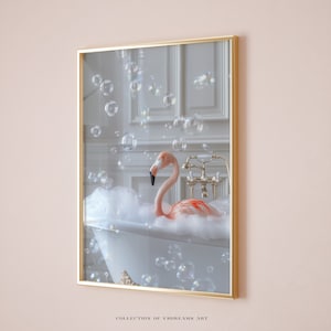 May include: A pink flamingo taking a bath in a white bathtub with bubbles floating around it. The bathtub is in a white bathroom with gold fixtures. The image is framed in a gold frame.