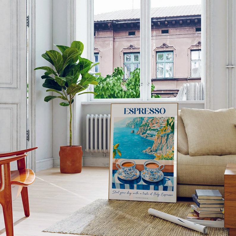 May include: A poster with a blue and white illustration of a coastal town in Italy with two cups of espresso on a blue and white striped tablecloth. The poster has the text "Espresso" in blue and white letters and the text "Start your day with a taste of Italy Espresso" in smaller blue and white letters.