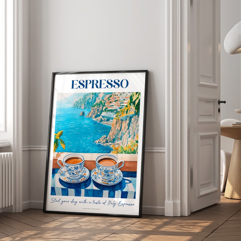 May include: A black framed poster with a colorful illustration of a coastal Italian town with two cups of espresso on a blue and white striped tablecloth. The text on the poster reads "Espresso. Start your day with a taste of Italy Espresso."