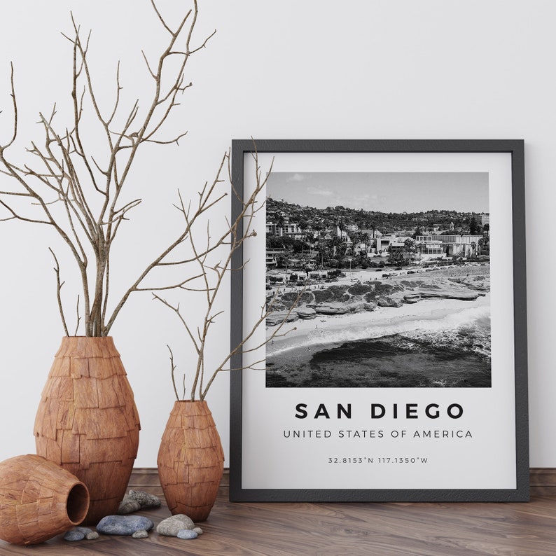 Może przedstawiać: Czarno-białe zdjęcie plaży w San Diego w Kalifornii. Zdjęcie jest oprawione w czarną ramę i zawiera napis "San Diego, Stany Zjednoczone Ameryki, 32.8155&deg;N 117.1550&deg;W" wydrukowany pod obrazem.