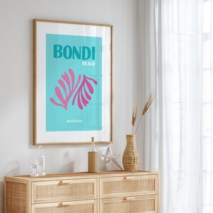 May include: A framed poster with a blue background and pink stylized leaves. The poster says "Bondi Beach Australia".