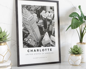 May include: Black and white aerial photograph of Charlotte, North Carolina, with the city's skyline in the center. The text "CHARLOTTE", "UNITED STATES OF AMERICA", and "35.2087°N 80.8307°W" is printed below the image.