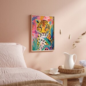 May include: A colorful painting of a leopard with a pink, blue, and green background. The leopard is looking directly at the viewer with a serious expression. The painting is framed in a white frame.