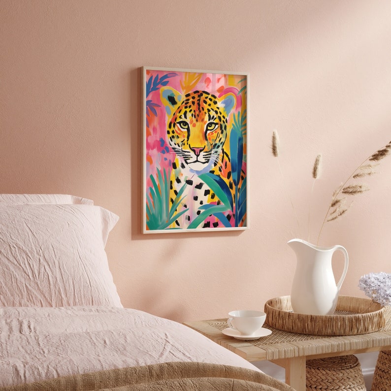 May include: A colorful painting of a leopard with a pink, blue, and green background. The leopard is looking directly at the viewer with a serious expression. The painting is framed in a white frame.