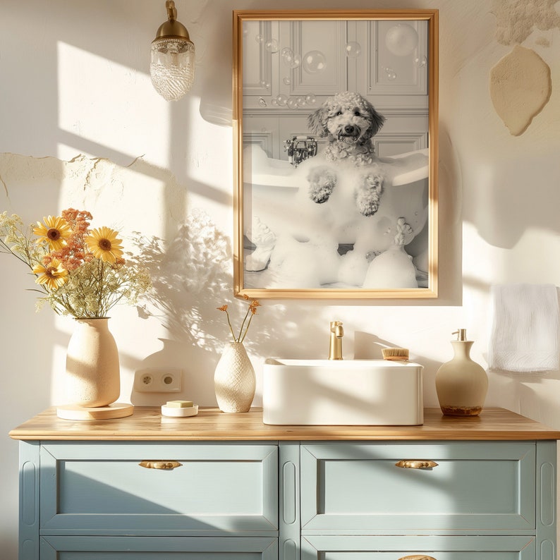 May include: A white fluffy dog sits in a bathtub filled with bubbles. The dog is smiling and looking at the camera. The photo is framed in a wooden frame and hanging on a white wall. The bathroom has a wooden vanity with a white sink and a towel hanging on the wall.