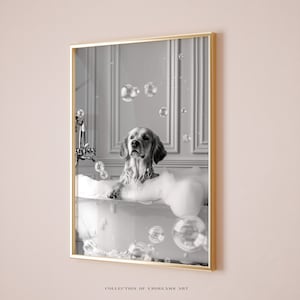 May include: A black and white photo of a golden retriever dog sitting in a bathtub full of bubbles. The dog is looking up at the camera with a playful expression. There are several soap bubbles floating in the air around the dog.