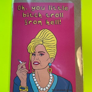 May include: A greeting card featuring a pop art style illustration of a woman with blonde hair, wearing a blue top, and a pearl necklace. The card has the text "Oh, you little bitch troll from hell!" on a pink background.