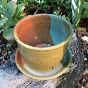 May include: A ceramic planter with a speckled glaze in shades of brown, yellow, and green. The planter has a saucer.