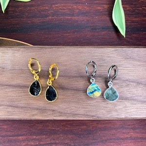 May include: Two pairs of drop earrings. The first pair features gold-tone hoops with black, teardrop-shaped stones. The second pair features silver-tone hoops with iridescent, teardrop-shaped stones displaying blue and yellow hues.