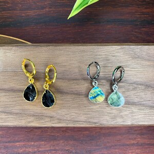 May include: Two pairs of teardrop-shaped earrings. One pair features black stones set in gold-toned metal hoops, while the other pair features iridescent, multi-colored stones set in silver-toned metal hoops, each with a hinged closure mechanism.