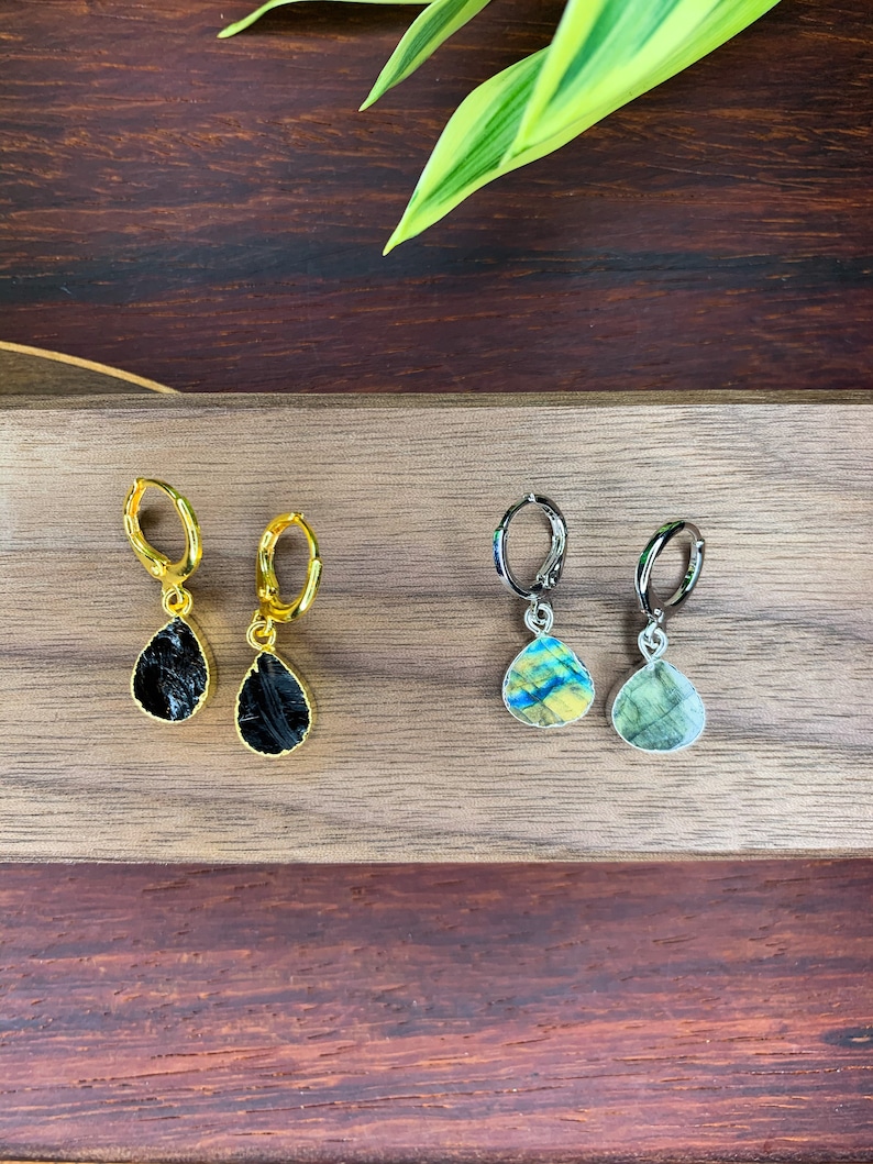 May include: Two pairs of teardrop-shaped earrings. One pair features black stones set in gold-toned metal hoops, while the other pair features iridescent, multi-colored stones set in silver-toned metal hoops, each with a hinged closure mechanism.