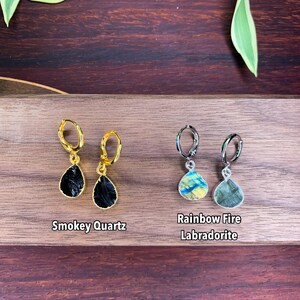 May include: Two pairs of hoop earrings with teardrop-shaped gemstone pendants. The left pair features black Smokey Quartz stones on gold-toned hoops, while the right pair features iridescent Rainbow Fire Labradorite stones on silver-toned hoops.