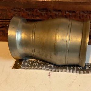 K&ouml;nnte beinhalten: Ein silberner Zinnbecher mit abgerundetem Boden und einem ausgestellten Rand. Der Becher hat ein Band um die Mitte.