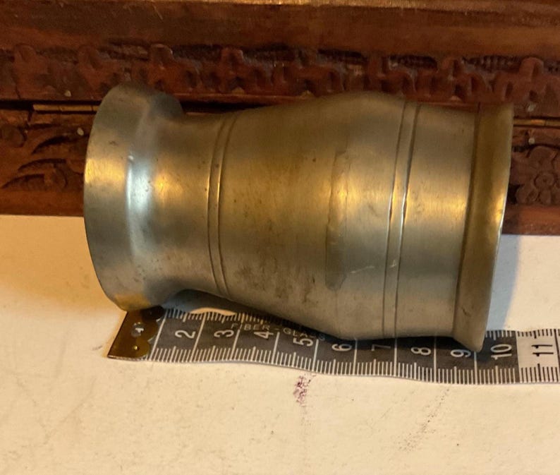 K&ouml;nnte beinhalten: Ein silberner Zinnbecher mit abgerundetem Boden und einem ausgestellten Rand. Der Becher hat ein Band um die Mitte.